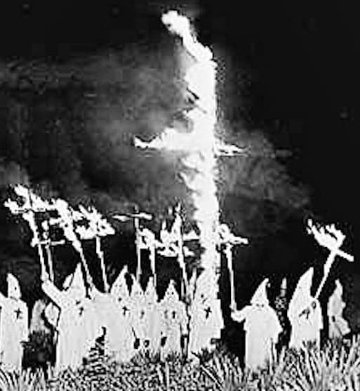 The Klan in hooded white sheets holding burning crosses.